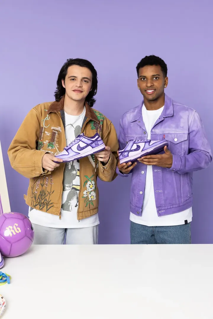 Dos chicos con chaquetas vaqueras pintadas y zapatillas moradas del drop de Rodrygo Goes con Juegaterapia